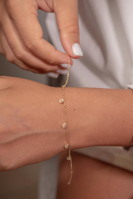 Woman wearing gold-plated 925 sterling silver bracelet with dangling drop-shaped clear zircon stones