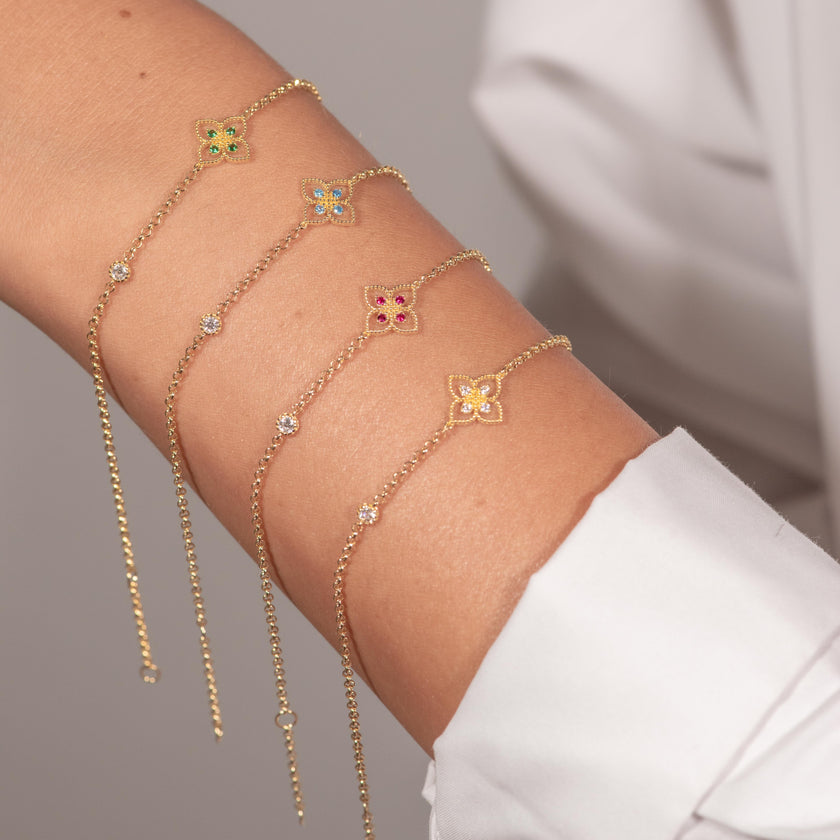 Woman wearing four gold-plated 925 sterling silver floral zircon chain bracelets stacked in blue, clear, green and pink